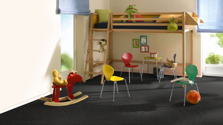 Hell gestaltetes Kinderzimmer mit Holz-Hochbett, bunten Stühlen und dunklen Teppichfliesen.