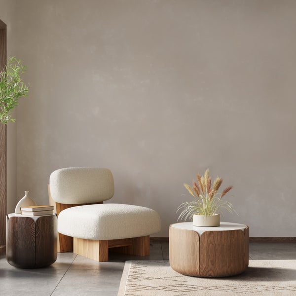 Modernes, minimalistisches Wohnzimmer mit hellem Polstersessel, Beistelltischen aus Holz und schlichter Wandgestaltung.