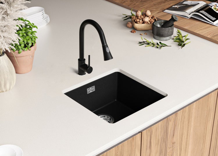 Schwarzes Küchenspülbecken mit Wasserhahn auf einer hellen Arbeitsplatte.