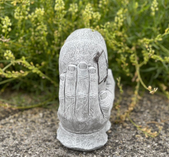 Steinfigur in Form von zwei schützenden Händen, die einen runden Stein halten, geeignet als Gartendekoration.