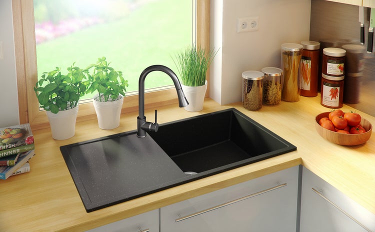 Schwarze Küchenspüle mit Armatur und Kräutern auf der Arbeitsplatte