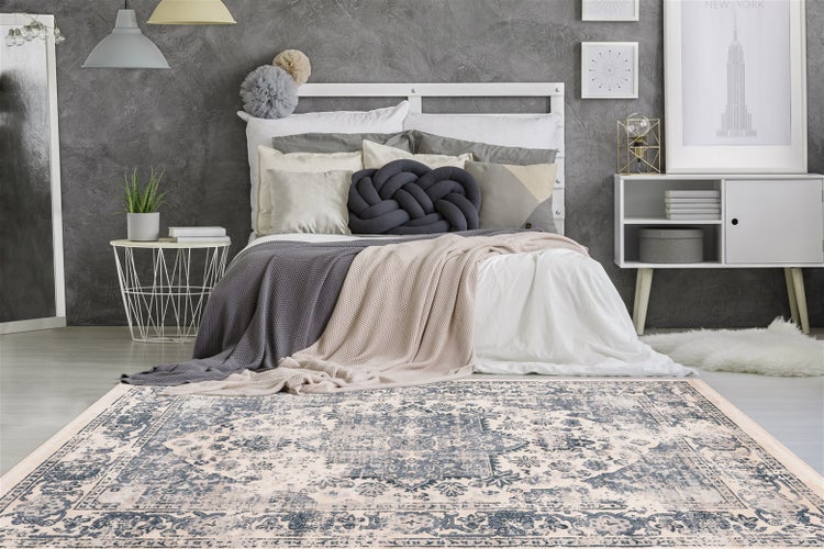 Modernes Schlafzimmer mit einem Orientteppich im Vintage-Stil, weißem Bettgestell, verschiedenen Dekokissen und einer grau strukturierten Wand.