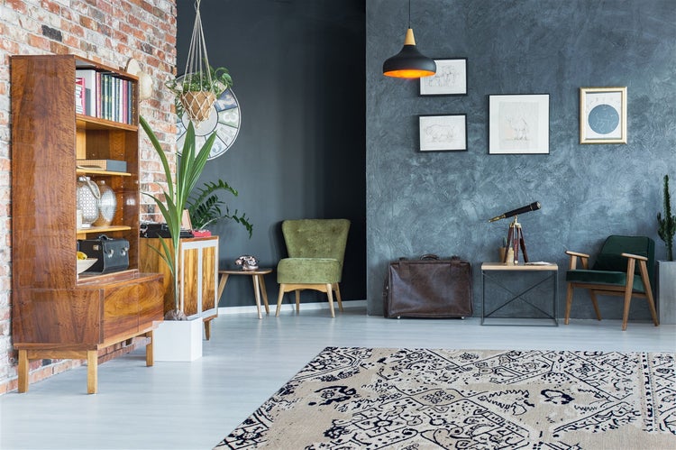 Helles Wohnzimmer im Vintage-Stil mit Backsteinwand, dunkler Strukturwand, Holzregal, grünen Samtsesseln und gemustertem Teppich.