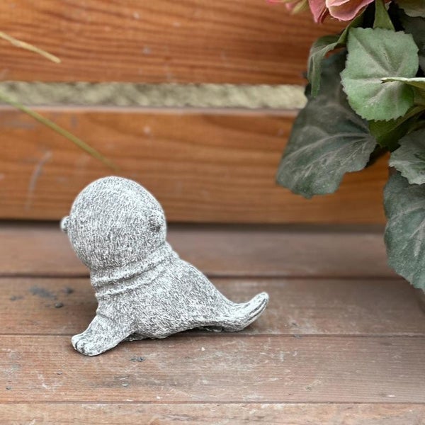 Kleine Gartenfigur in Robben-Optik aus Steinguss, sitzend auf Holzoberfläche.