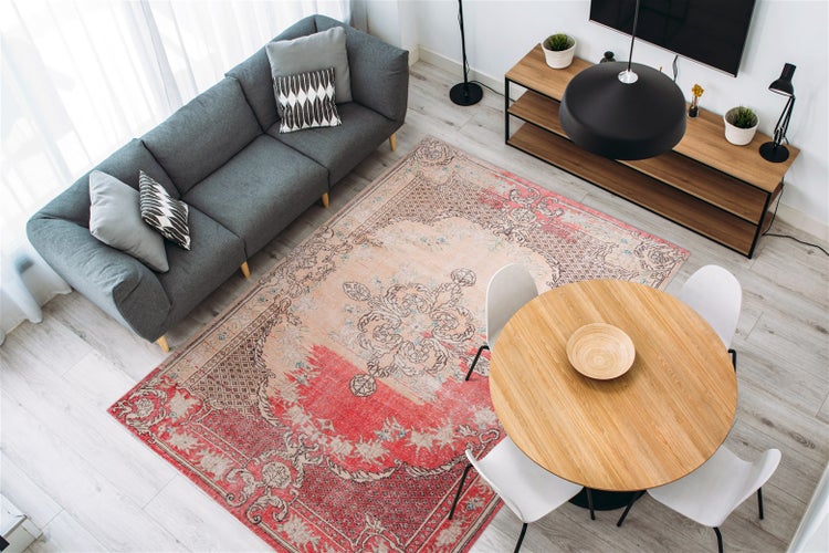 Heller, moderner Wohnbereich mit einem großen Orientteppich im Vintage-Stil, einem grauen Sofa und einem runden Holzesstisch mit weißen Stühlen.