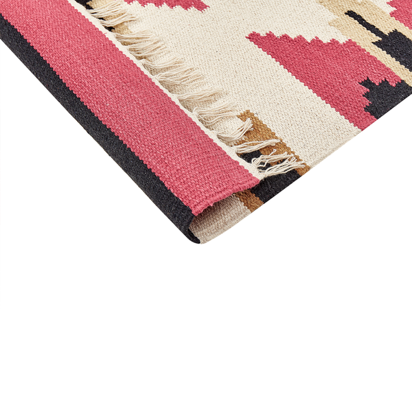 Nahaufnahme einer Ecke eines flachgewebten Teppichs mit geometrischem Muster in Pink, Schwarz und Beige sowie Fransen.