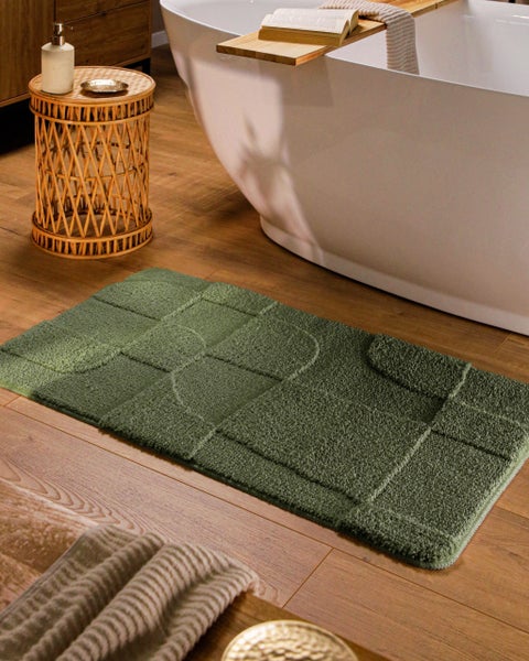 Rechteckige Badematte mit geometrischem Reliefmuster auf Holzfußboden vor einer Badewanne in einem modernen Badezimmer.