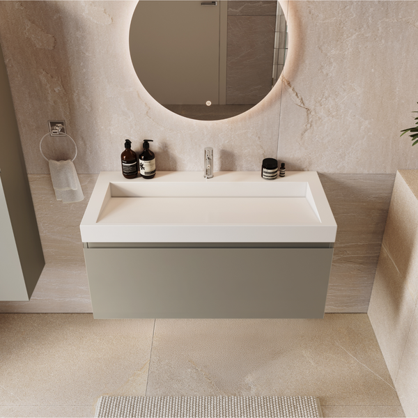 Modernes Badezimmer mit Waschtisch, wandhängendem Unterschrank, rundem LED Spiegel und Waschtischarmatur vor einer Natursteinoptik Wand.
