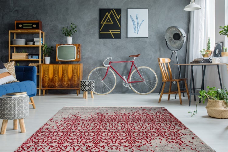 Gemusterter Teppich in einem modern eingerichteten Zimmer mit Vintage-Möbeln, Retro-Fernseher und rotem Fahrrad vor grauer Wand.