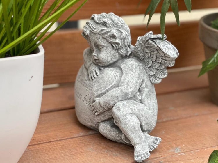 Steinfigur kleiner Engel schlafend auf einem Herz mit Inschrift Ein Engel schütze dich als Dekoration für Grab oder Garten