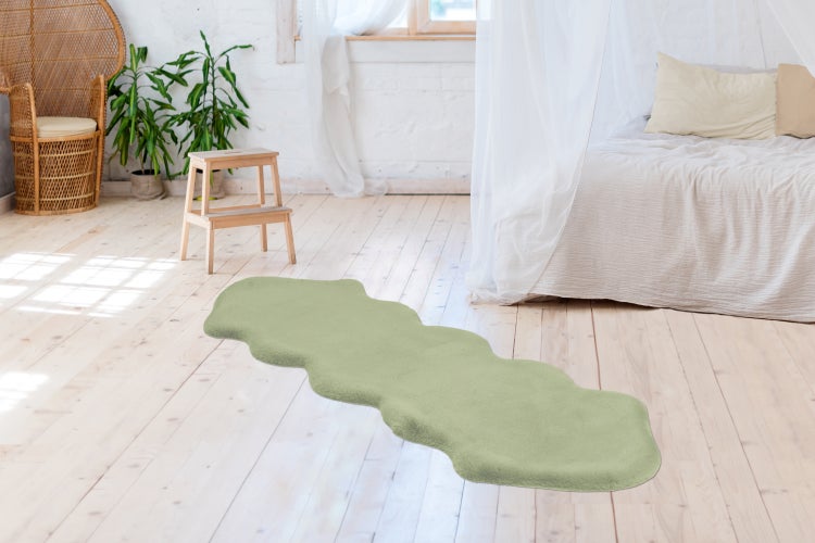 Länglicher, wellenförmiger Teppich in weicher Optik auf hellem Holzboden in einem hellen Schlafzimmer mit Bett und Korbsessel.