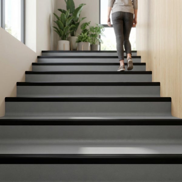 Treppenverkleidung mit rutschhemmenden Kantenprofilen in einem modernen Eingangsbereich mit Pflanzen und Person, die die Treppe hinaufgeht.