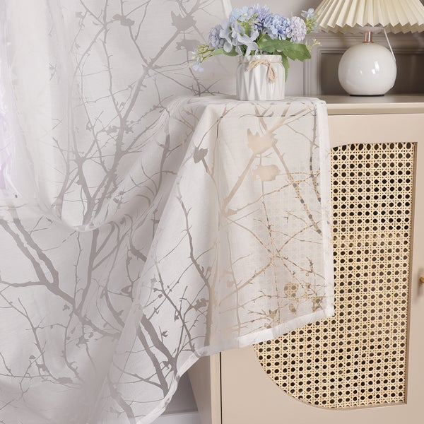 Dekoratives Interieur mit einem Schrank, einer Lampe, Blumen und einem transparenten Vorhang mit Zweigmuster.