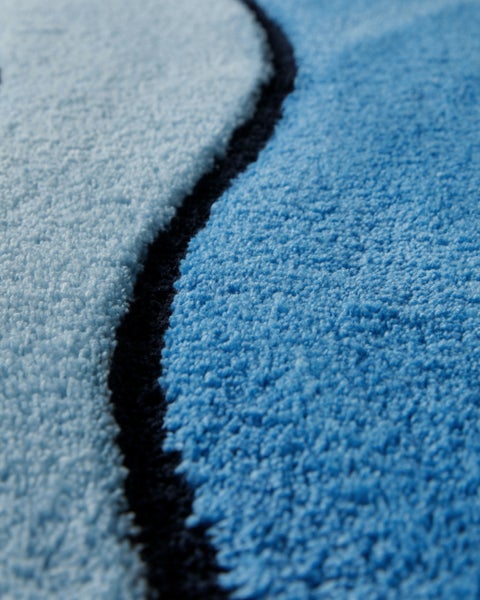 Nahaufnahme eines weichen Badteppichs in Blau mit Wellenmuster und Hochflor.