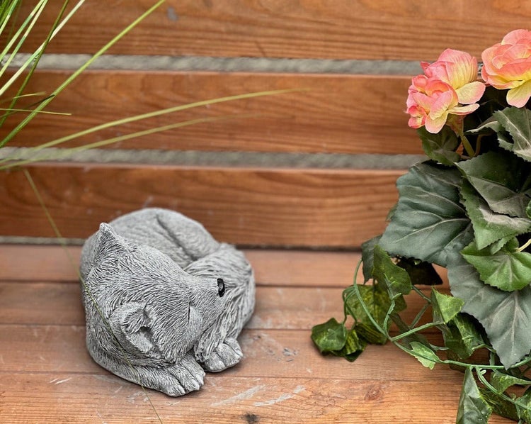 Schlafende Wolf-Steinfigur als Gartendekoration auf einer Holzbank neben einer Pflanze.