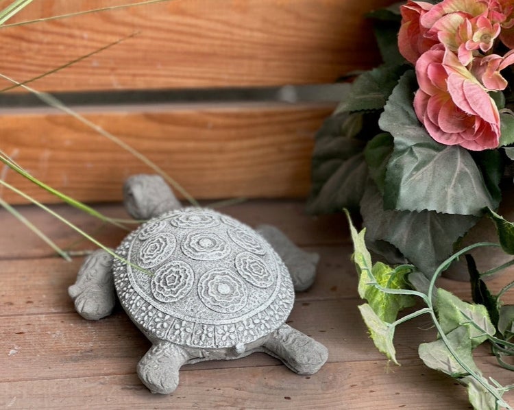 Gartendeko-Schildkröte aus Stein mit gemustertem Panzer, platziert auf Holz neben einer Pflanze