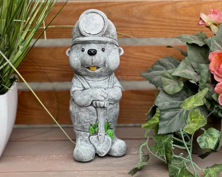 Gartenfigur in Steinoptik in Form eines Tieres mit Helm und Schaufel, dekoriert zwischen Pflanzen.