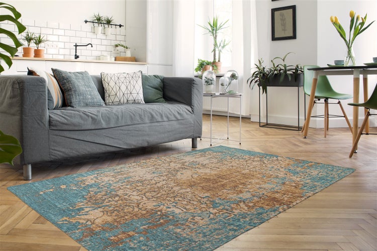 Rechteckiger Teppich mit Vintage-Muster in Blau und Beige auf Fischgrätparkett in einem hellen Wohnzimmer mit grauem Sofa.