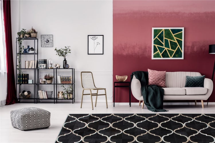 Moderner Wohnraum mit rot-weiß gestalteter Wand, hellem Sofa, schwarzem Metallregal, goldenem Metallstuhl und gemustertem Teppich.