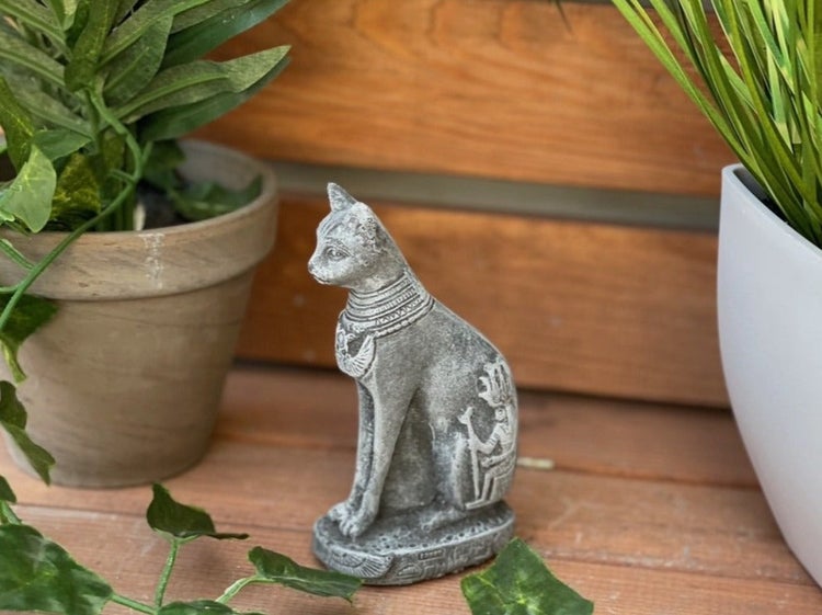 Dekorative Katzenfigur im altägyptischen Stil aus Stein für den Innen- und Außenbereich auf Holzuntergrund zwischen zwei Pflanzen