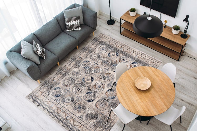 Modernes, helles Wohn- und Esszimmer mit einem großen Teppich mit Vintage-Orient-Muster, grauem Sofa und rundem Esstisch aus Holz.