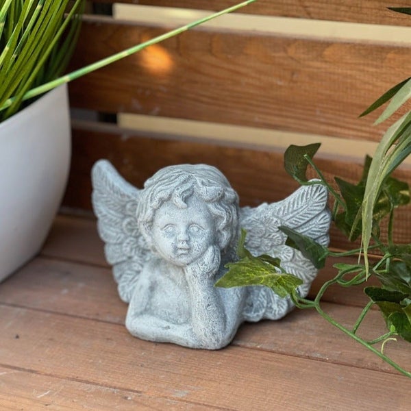 Steinfigur Engel als Gartendekoration auf einer Holzoberfläche mit Pflanzen platziert.
