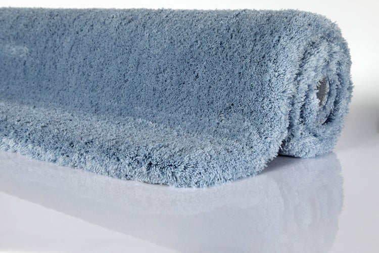 Hochfloriger blauer Teppich oder Badematte, teilweise eingerollt, mit dichter Struktur.