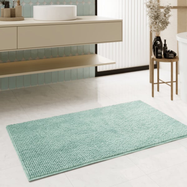 Badematte mit Chenille-Struktur vor einem modernen Waschtisch im hellen, organisierten Badezimmer.