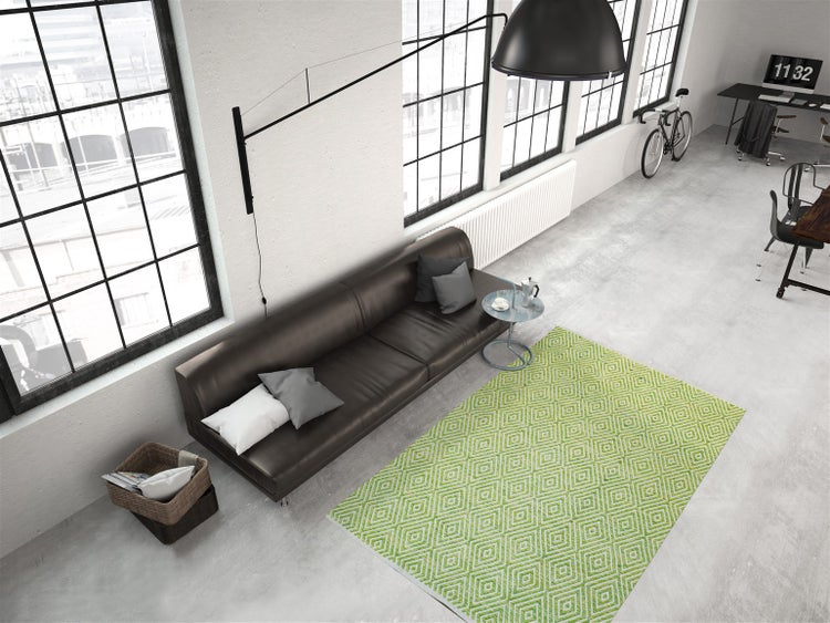 Moderner Wohnraum im Industriestil mit dunklem Ledersofa, grünem Teppich mit geometrischem Muster, Betonboden und großen Fenstern.