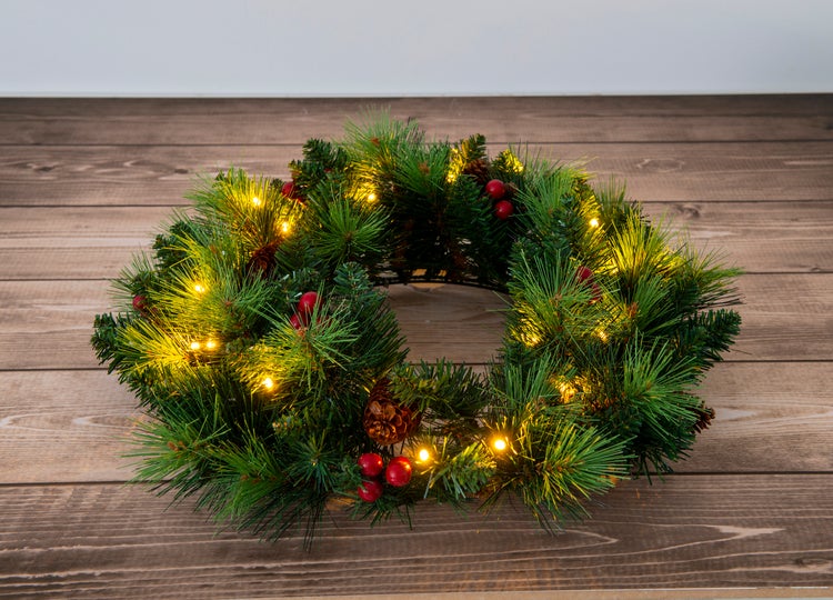 Weihnachtlicher Türkranz mit Beleuchtung, Tannenzweigen, roten Beeren und Zapfen