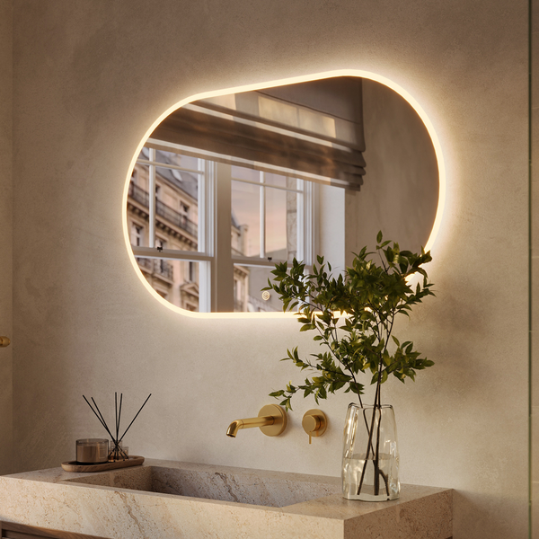 Organisch geformter Wandspiegel mit LED Beleuchtung über einem Waschbecken aus Stein in einem modernen Badezimmer.