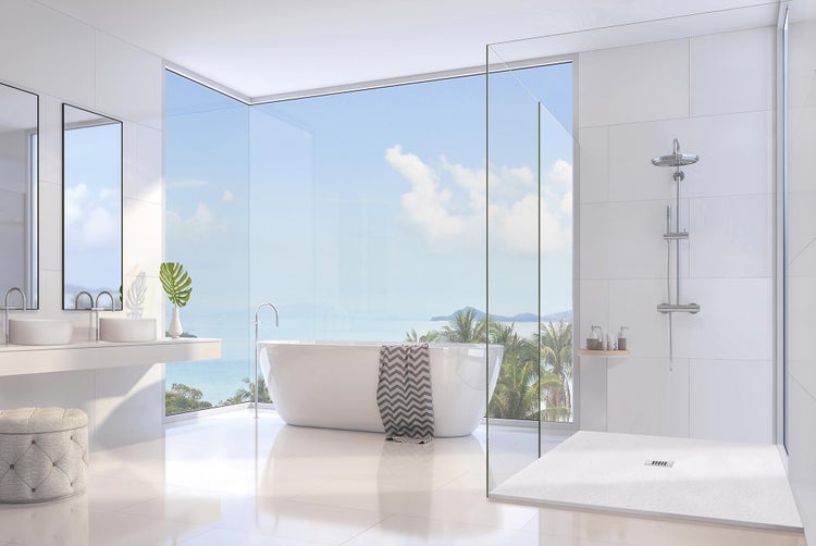 Modernes, helles Badezimmer mit freistehender Badewanne, bodengleicher Dusche und großem Eckfenster mit Ausblick auf das Meer.