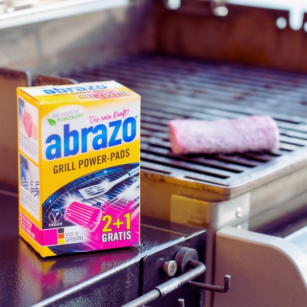Packung abrazo Grill Power-Pads auf einem Grill mit einem Reinigungsschwamm auf dem Grillrost.