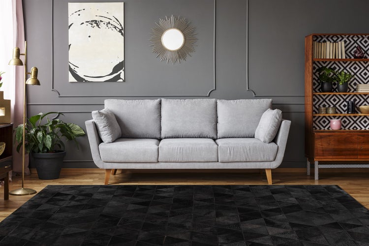 Modernes Wohnzimmer mit grauem Dreisitzer-Sofa, schwarzem Teppich mit geometrischem Muster, Holzregal und dunkelgrauer Wand mit Zierleisten.
