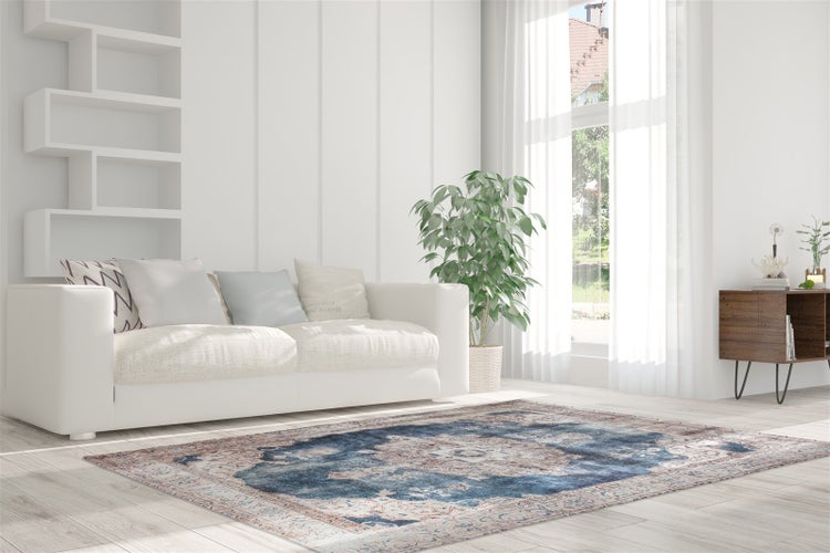 Helles Wohnzimmer mit weißem Sofa, orientalisch gemustertem Teppich, grüner Zimmerpflanze und großem Fenster mit hellen Vorhängen.