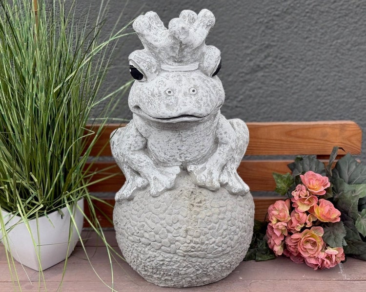 Gartenfigur Froschkönig aus Stein mit Krone, sitzend auf einer strukturierten Kugel.