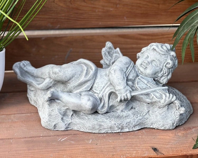 Gartendekoration aus Stein in Form eines liegenden Engels mit einer Geige.