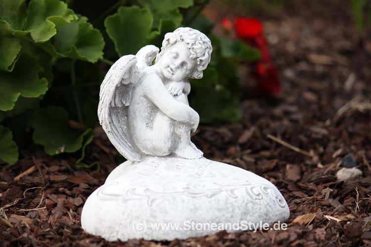 Gartenfigur Engel sitzend auf einem Herz aus Stein als Dekoration fuer den Garten