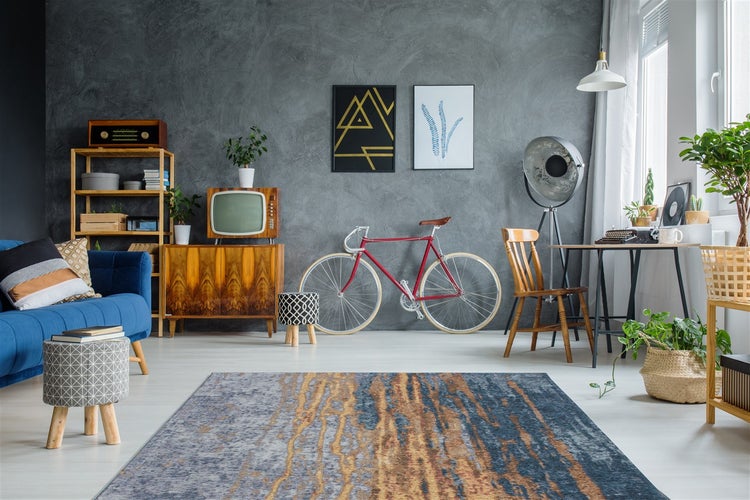 Modernes Wohnzimmer mit gemustertem Teppich, strukturierter grauer Wand, Vintage-Möbeln, rotem Fahrrad und industrieller Stehlampe.