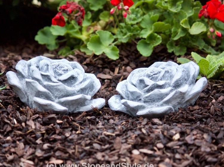 Zwei dekorative Rosenblüten aus Stein als Gartenfigur im Blumenbeet.