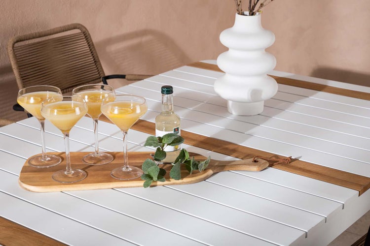 Szene mit vier gefüllten Cocktailgläsern auf einem Holzbrett, einer Limonadenflasche und einer weißen Blumenvase auf einem Gartentisch