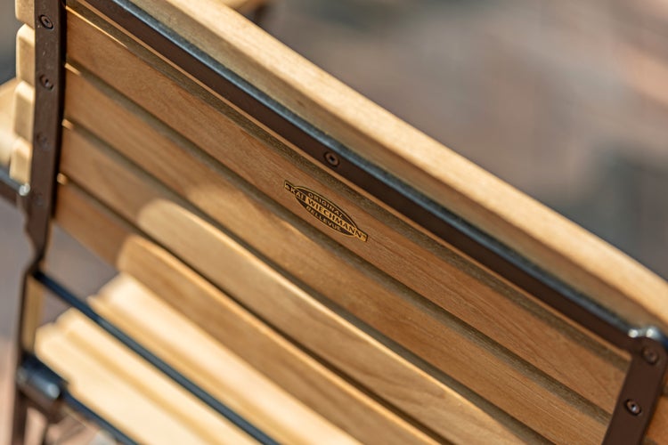 Detailansicht der Rückenlehne einer Gartenbank aus Holz mit Metallrahmen und dem Logo von Kai Wiechmann Bellevue.