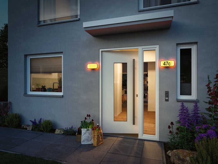 Modernes Haus mit geöffneter Haustür, Hausnummerleuchte und Einkaufstüten vor der Tür