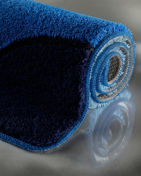 Nahaufnahme einer eingerollten, flauschigen Badmatte mit weicher Textur und rutschhemmender Rückseite.
