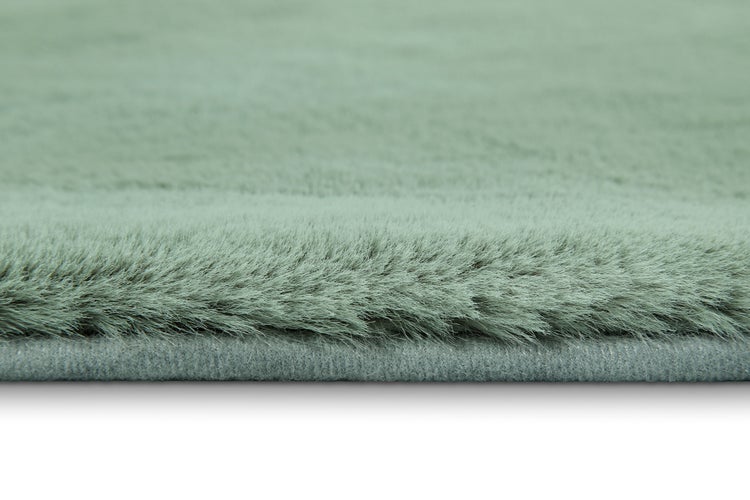 Detailaufnahme eines weichen Hochflor-Teppichs in Grün mit dichter Faserstruktur und grauer Kante.