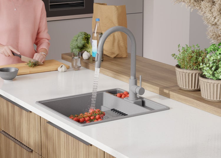 Küchenspüle mit Wasserhahn und gewaschenen Tomaten auf einem Abtropfgitter, umgeben von Lebensmitteln und Kräutern.