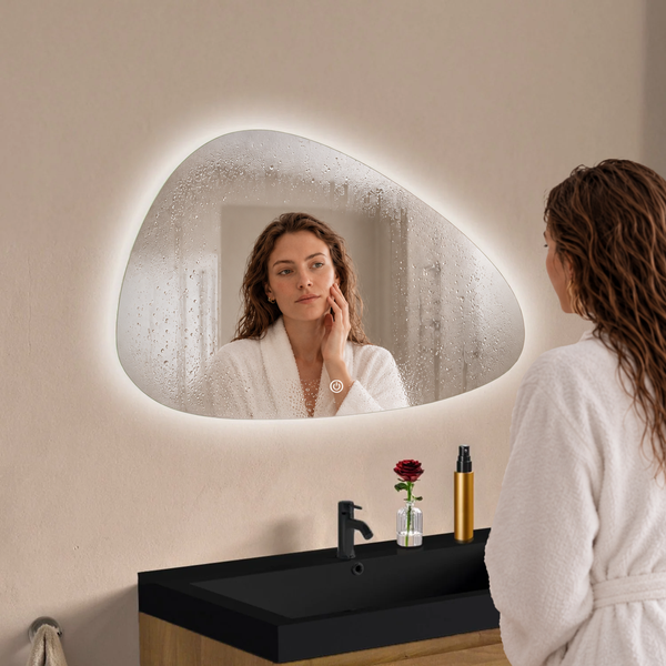 Organisch geformter Badezimmerspiegel mit LED Beleuchtung und Touchschalter über einem Waschplatz mit dunklem Waschbecken.