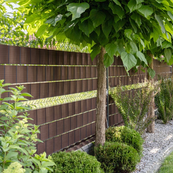 Sichtschutzstreifen in einem Doppelstabmattenzaun in einer Gartenlandschaft mit Bäumen und Sträuchern