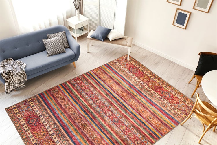 Gemusterter Teppich mit orientalischen Motiven und Streifen in einem hellen Wohnzimmer mit Sofa und Holzboden.