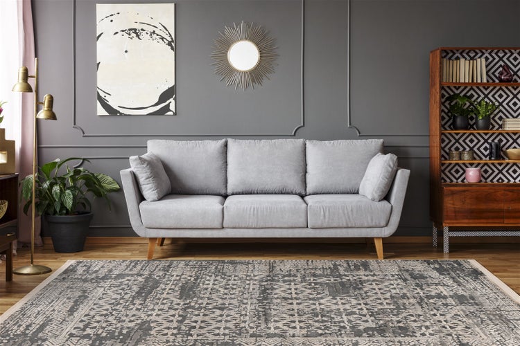 Modernes Wohnzimmer mit grauem Dreisitzer-Sofa, gemustertem Teppich, Holzregal und dunkelgrauer Wand mit dekorativen Zierleisten und Spiegel.